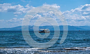 Fishing boat sails in waving sea, cloudy blue sky background