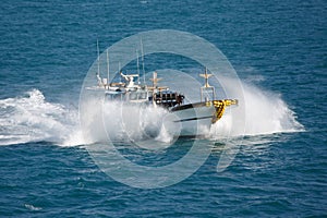 Fishing boat in sea splashes, floats with high speed