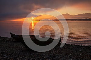 Fishing boat on the shore of the lake. Colorful sunrise on the sky