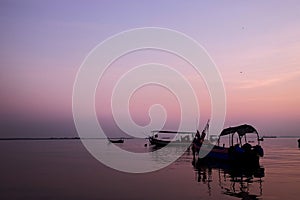 Fishing boat silhouette with orange sunrise sky and water reflection