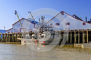 Fishing boat stands near the pier near the warehouses, a white s