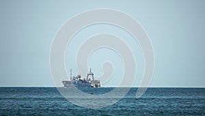 Fishing boat trawler catches fish while sailing on sea. A commercial fishing boat on the horizon in a distance sail to