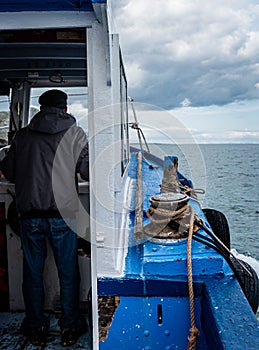 Fishing boat, view of both cabin and sea, being sailed by an old fisherman visible from behind shows hardships of fishermen at sea