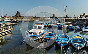 Fishing boats lined up in the harbour of Aci Trezza, Sicily with stacks of Isole dei Ciclopi in the background