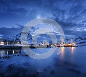 Fishing boats near pier on the sea and snowy mountains at night