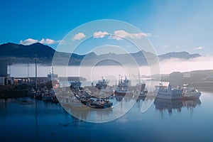 Fishing boats on a pier in blue fog in an early sunny morning in the summer