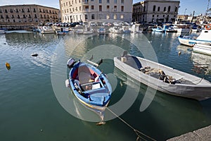 Fishing boats on the water in Ortigia island with the cityscape of Syracuse in Sicily, Italy