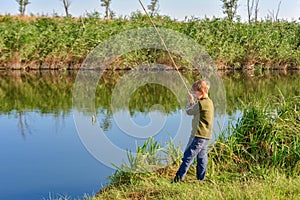 A fishing boy on a river holds a fishing rod, a child caught a fish and pulls it out of the water on a hook