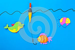 Fishing concept. Colorful toy fish with a hook and fishing buoy on blue background.