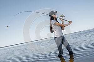 Fishing concept. Young fisherwoman makes a cast on background of skewed horizon line