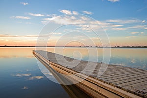 Fishing dock on a lake at sunrise with soft wispy clouds