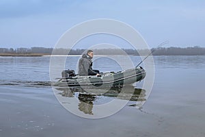 Fishing. Fisherman on inflatable boat with fishing tackle at lake in winter