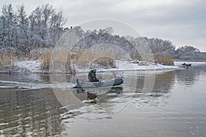 Fishing. Fisherman on inflatable boat with fishing tackle at lake in winter