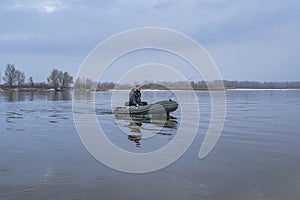 Fishing. Fisherman on inflatable boat with fishing tackle at lake in winter