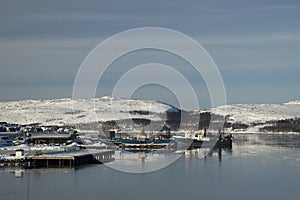 Fishing fleet in harbor with snow covered hills in background