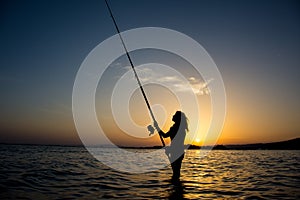 Fishing girl silhouette in the sea at sunset