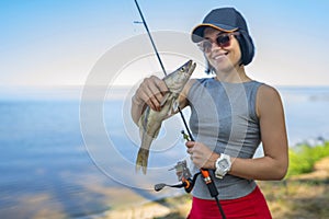 Fishing. Happy fisher girl with walleye zander fish trophy at lake shore