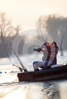 Fishing on ice- Fisherman sitting on frozen lake and drink tea