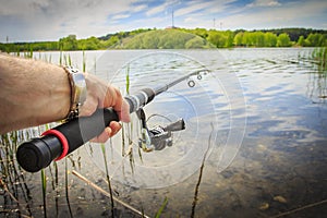 Fishing on lake. Fishing rod in fisherman`s hand against lake in summer in nature on bright sunny day