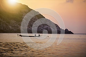 Fishing man on floating long tail boat behind island and sunset