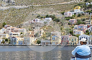 A Fishing Man Sitting on a Chair by the Main Port of Symi, Greece, With His Fishing Rod