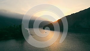 Fishing motor boat at sunrise. The sun's rays appear between the mountains and illuminate the fishing bay of the river