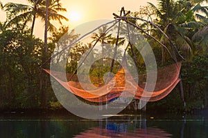 Fishing net glowing red, raised at sunset in Kerala, India