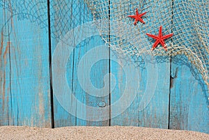 Fishing net and red starfishes against an old wooden background