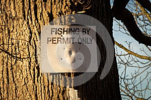 Fishing by permit only sign attached to a large tree in the winter sun