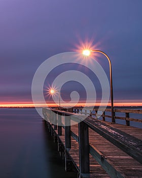 A fishing pier during dusk lit up by lamp posts. Blue hour moody purple sky - Long Island NY