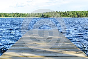 The fishing pier at the lake in rural Finland. Wooden pier at blue water and green forest on sunny day. Wooden jetty bridge