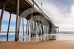 The fishing pier in Ocean City Maryland with sky and pier reflections shown underneath it.