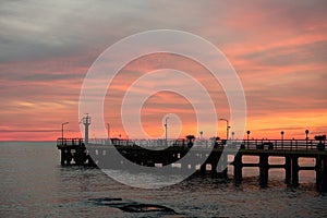 Fishing pier on the ocean with a colorful and golden sunset. Ocean beach sunrise and dramatic colorful sky clouds.