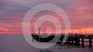 Fishing pier on the ocean with a colorful and golden sunset. Ocean beach sunrise and dramatic colorful sky clouds.