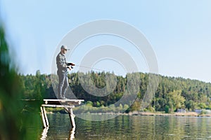 Fishing for pike, perch, carp. Fisherman with rod, spinning reel on river bank. Man catching fish, pulling rod while fishing on