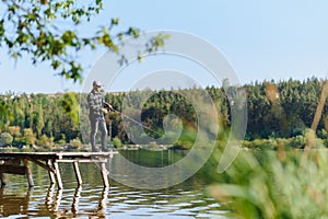 Fishing for pike, perch, carp. Fisherman with rod, spinning reel on river bank. Man catching fish, pulling rod while fishing on