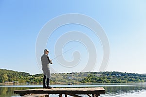 Fishing for pike, perch, carp. Fisherman with rod, spinning reel on river bank. Man catching fish, pulling rod while fishing on