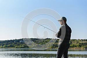 Fishing for pike, perch, carp. Fisherman with rod, spinning reel on river bank. Man catching fish, pulling rod while fishing on