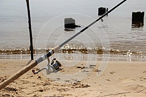 Fishing pole with reel and fishing line stands at the shore