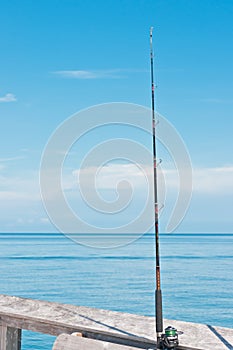 Fishing pole wedged in place between wood railing and bench  in tropical waters