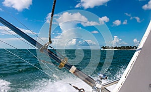 Fishing poles on deep sea fishing boat with view of island in distance under blue skies with fluffy white clouds