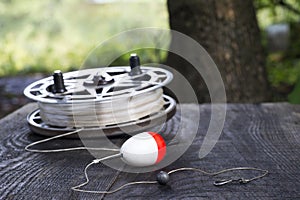 Fishing reel with fishing line, red and white float, hook and sinker on wooden table on natural background