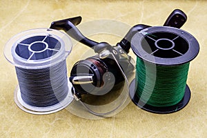 Fishing reel and spools of cords on the background of tarpaulin. Green and gray fishing line. Spools of braided fishing line