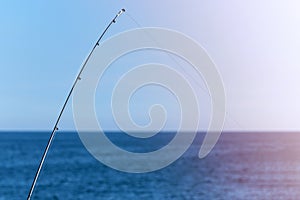 Fishing rod against blue ocean or sea background, copy space. Waiting for biggest haul. Meditative relax sport