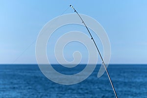 Fishing rod against blue ocean or sea background, copy space. Waiting for biggest haul. Meditative relax sport