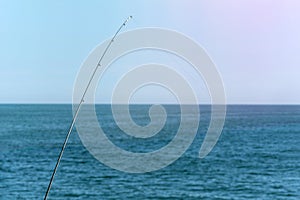 Fishing rod against blue ocean or sea background, copy space. Waiting for biggest haul. Meditative relax sport