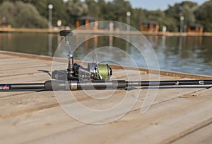 Fishing rod or angler closeup on wood coast over river or lake in summer