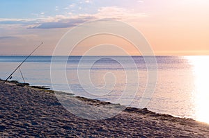 Fishing rod on the beach, sunrise reflected on the watery surface, horizon calm. sea shore