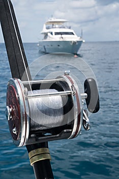 Fishing rod on a boat over blue sky and white sailing boat in the sea