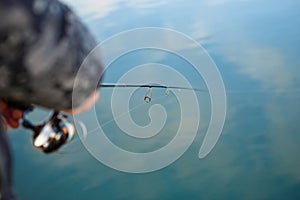 Fishing rod in the hands of a fisherman on the lake.